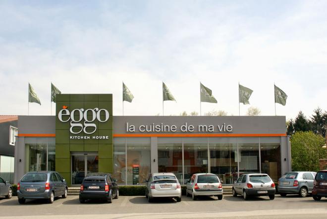Façade d'un magasin èggo avec des voitures garées devant et des drapeaux verts flottant sur le toit.