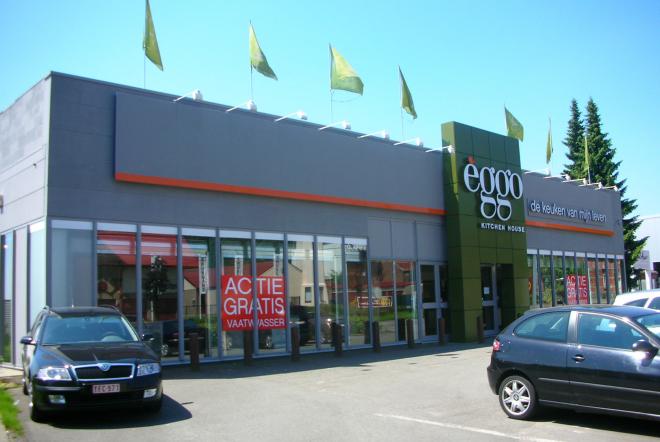 Façade d'un magasin èggo avec des voitures garées devant, enseigne verte et fenêtres alignées sur un bâtiment gris.