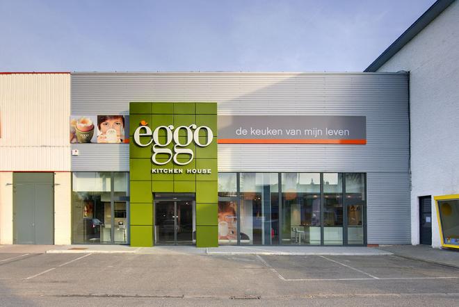 Façade d'un magasin èggo avec un panneau vert et des vitrines, entouré d'un parking vide sous un ciel dégagé.