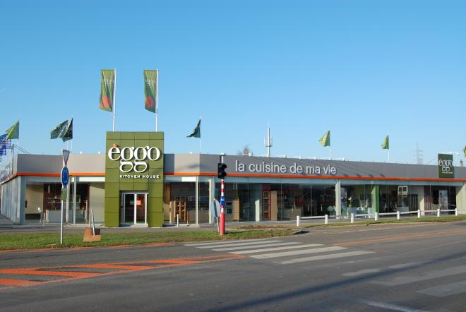 Façade du magasin èggo à La Louvière avec enseignes et drapeaux verts sur fond de ciel bleu.