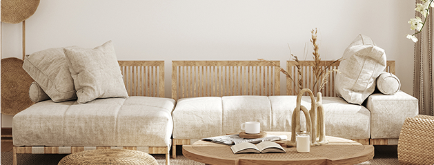Canapé en tissu beige avec coussins, table basse en bois avec livres et tasse, décoration en osier et plantes sèches.