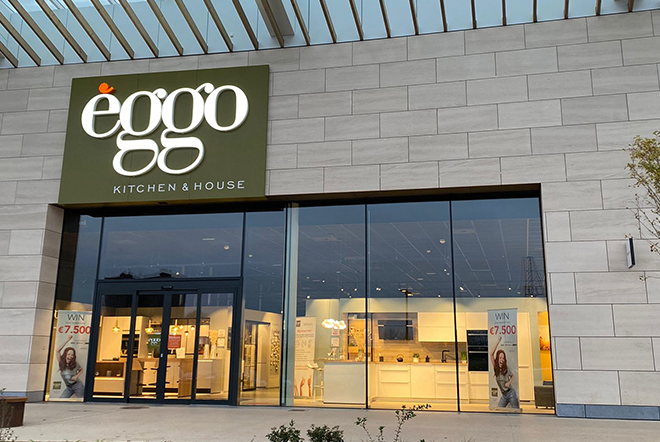 Façade d'un magasin èggo avec vitrines illuminées, logo blanc sur fond vert, et affiches promotionnelles à l'entrée.