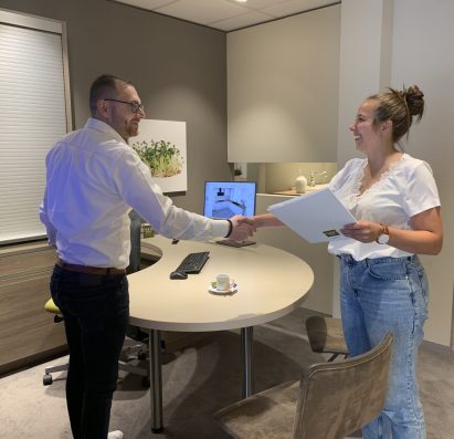validation rendez-vous Deux personnes se serrent la main dans un bureau moderne avec un ordinateur, des dossiers et une tasse de café sur la table.